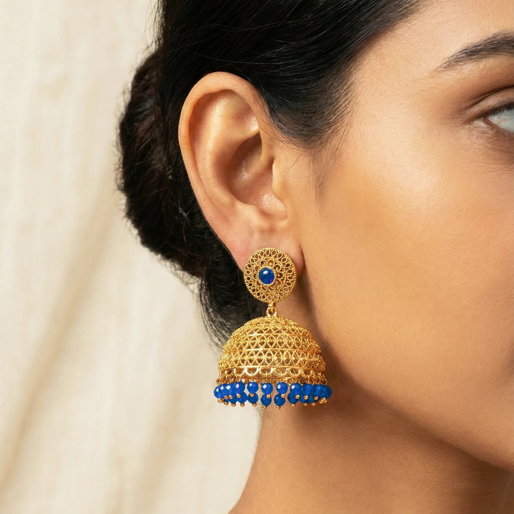Gold and blue earrings worn by a person with a neutral background