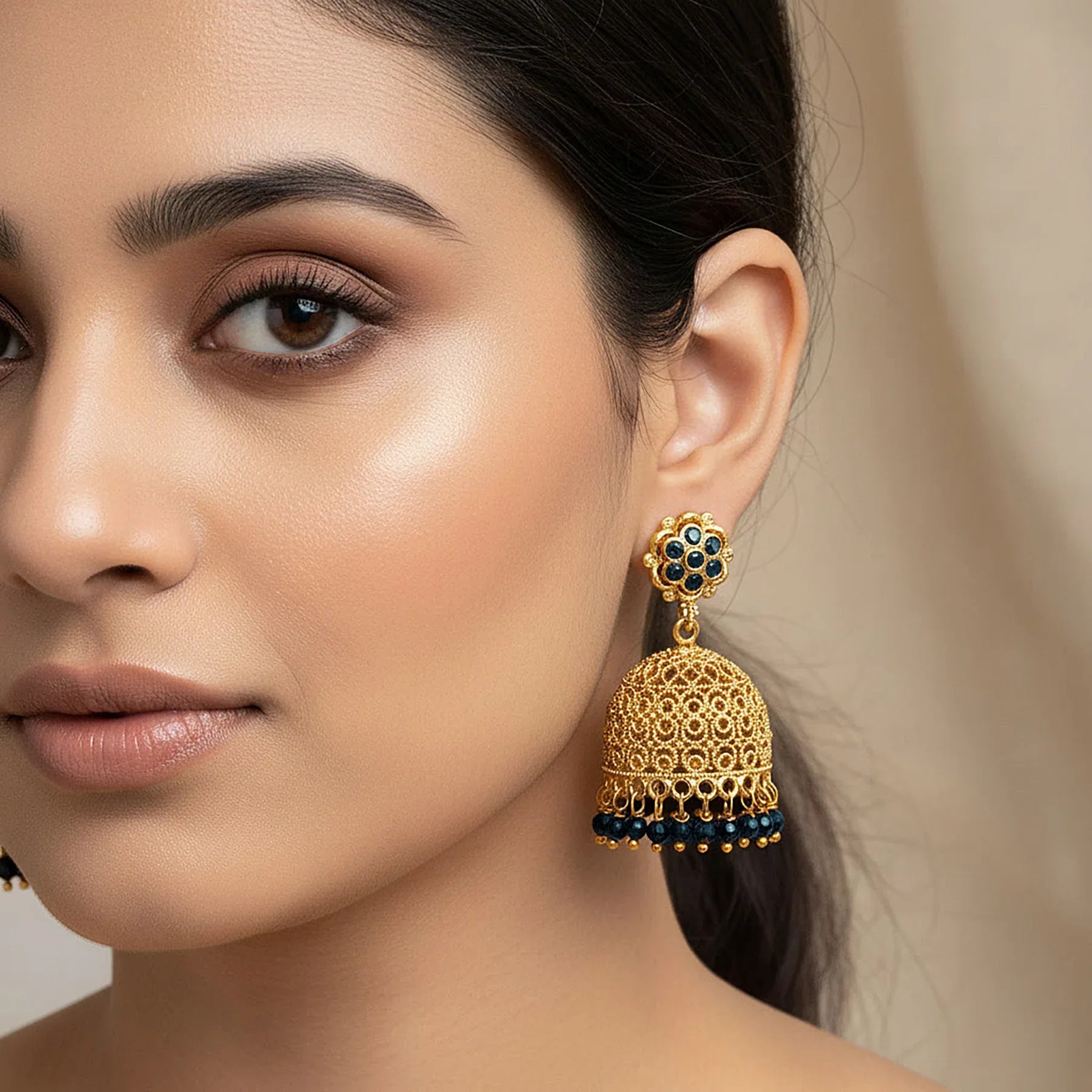 Close-up of a woman wearing gold and blue beaded earrings against a neutral background
