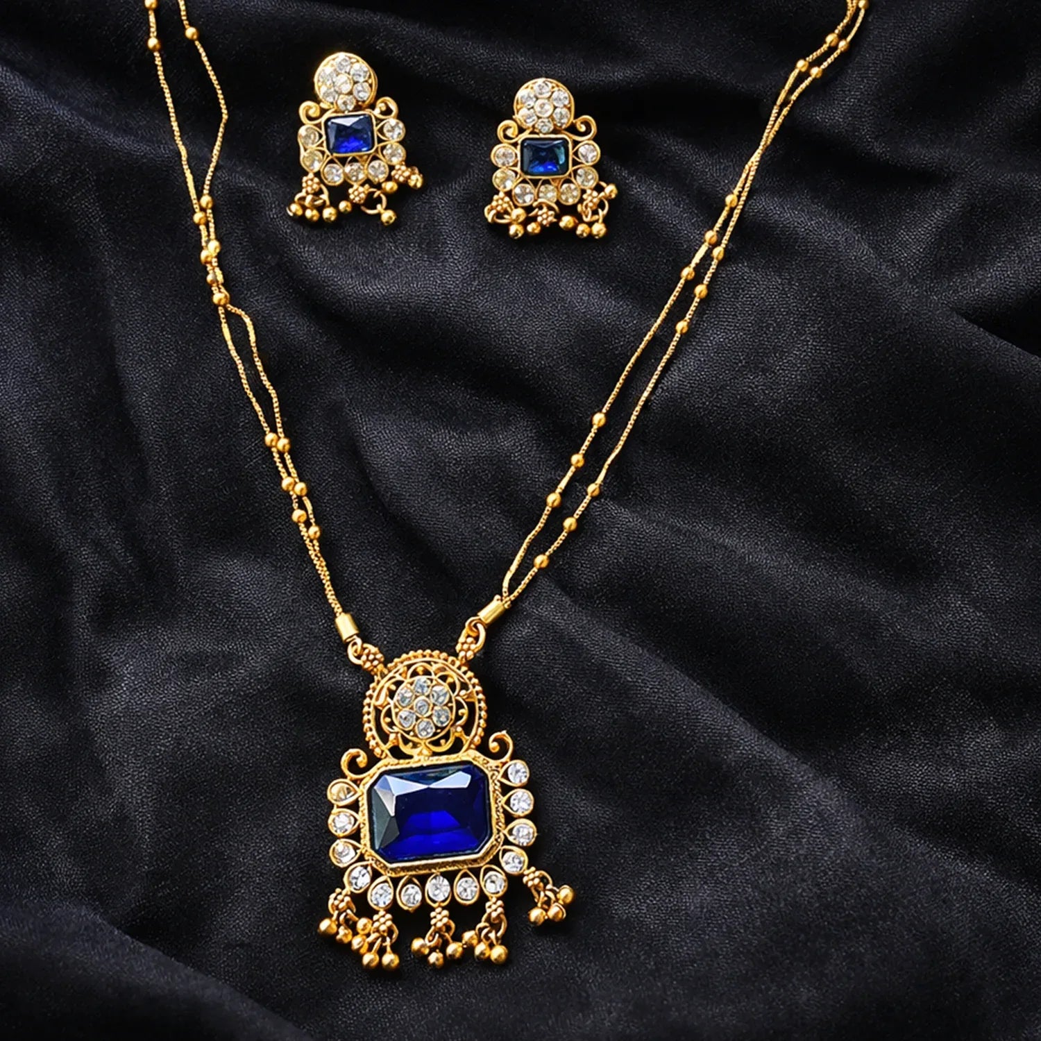 Gold necklace and earrings with blue gemstones on a black fabric background