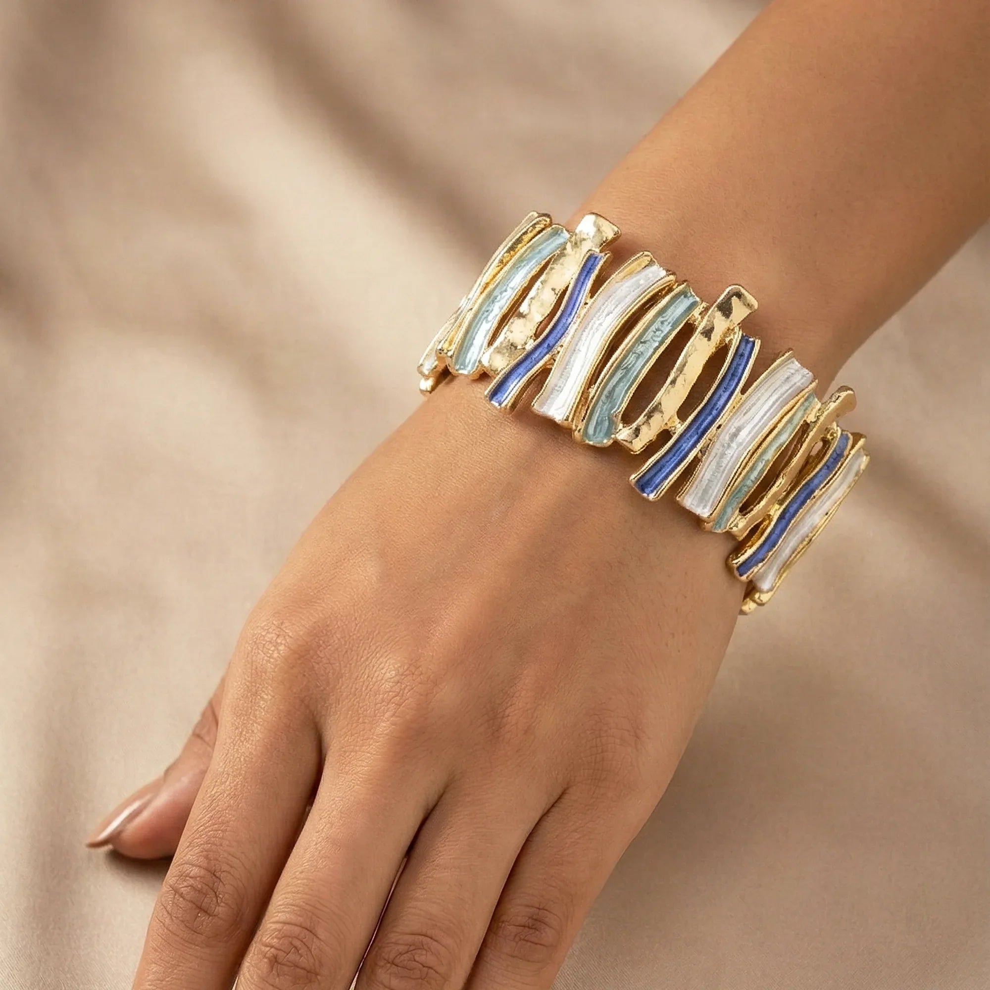 Gold bracelet with blue and white accents on a hand against a beige background
