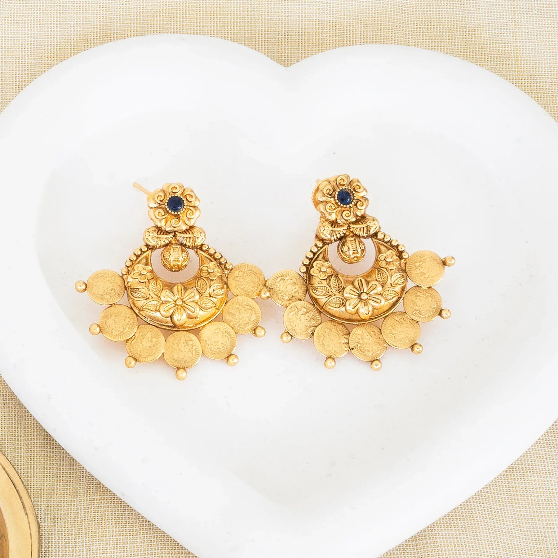 Gold earrings with intricate designs on a white heart-shaped pad