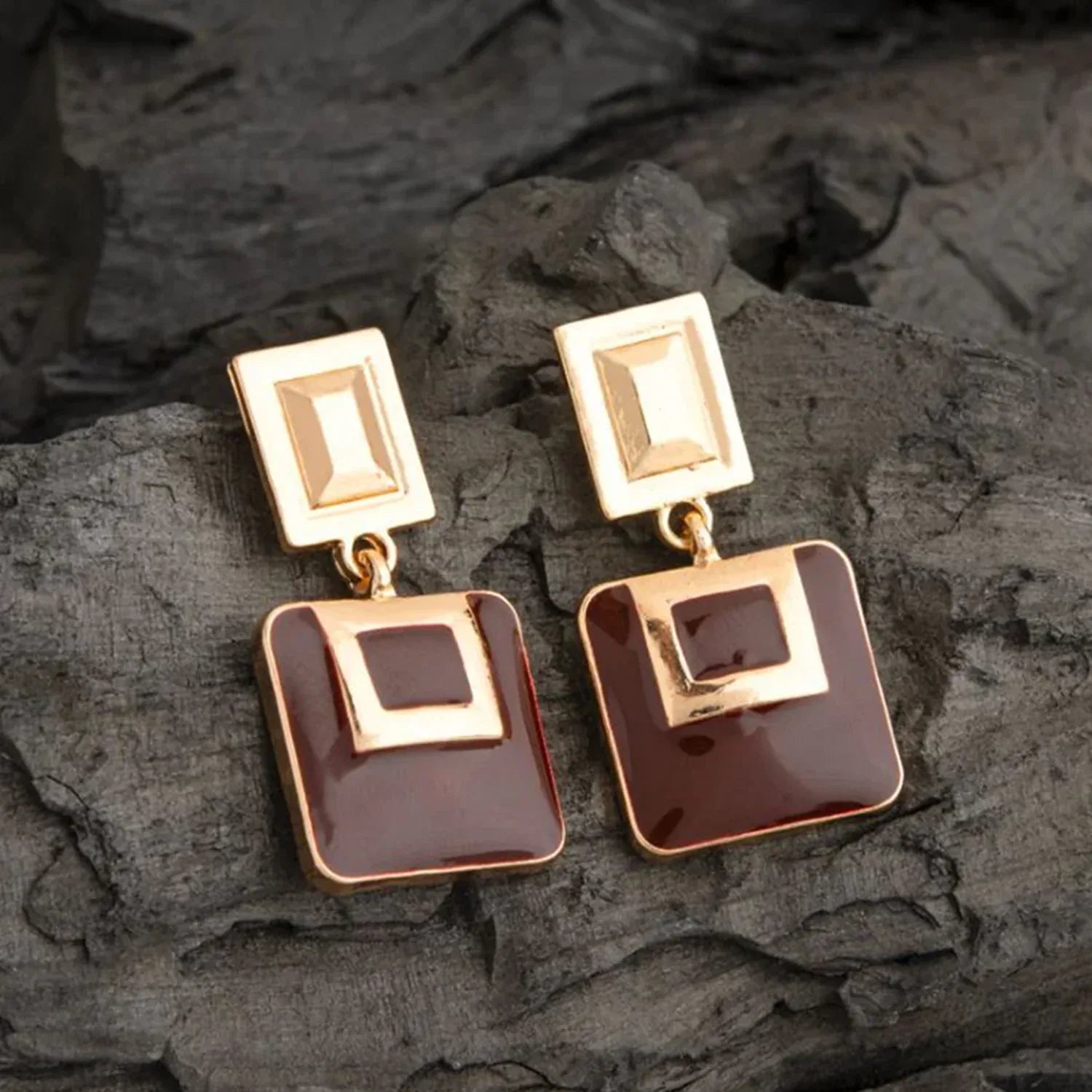 Gold and brown square earrings on a dark stone surface