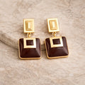 Gold and brown square earrings on a beige stone surface