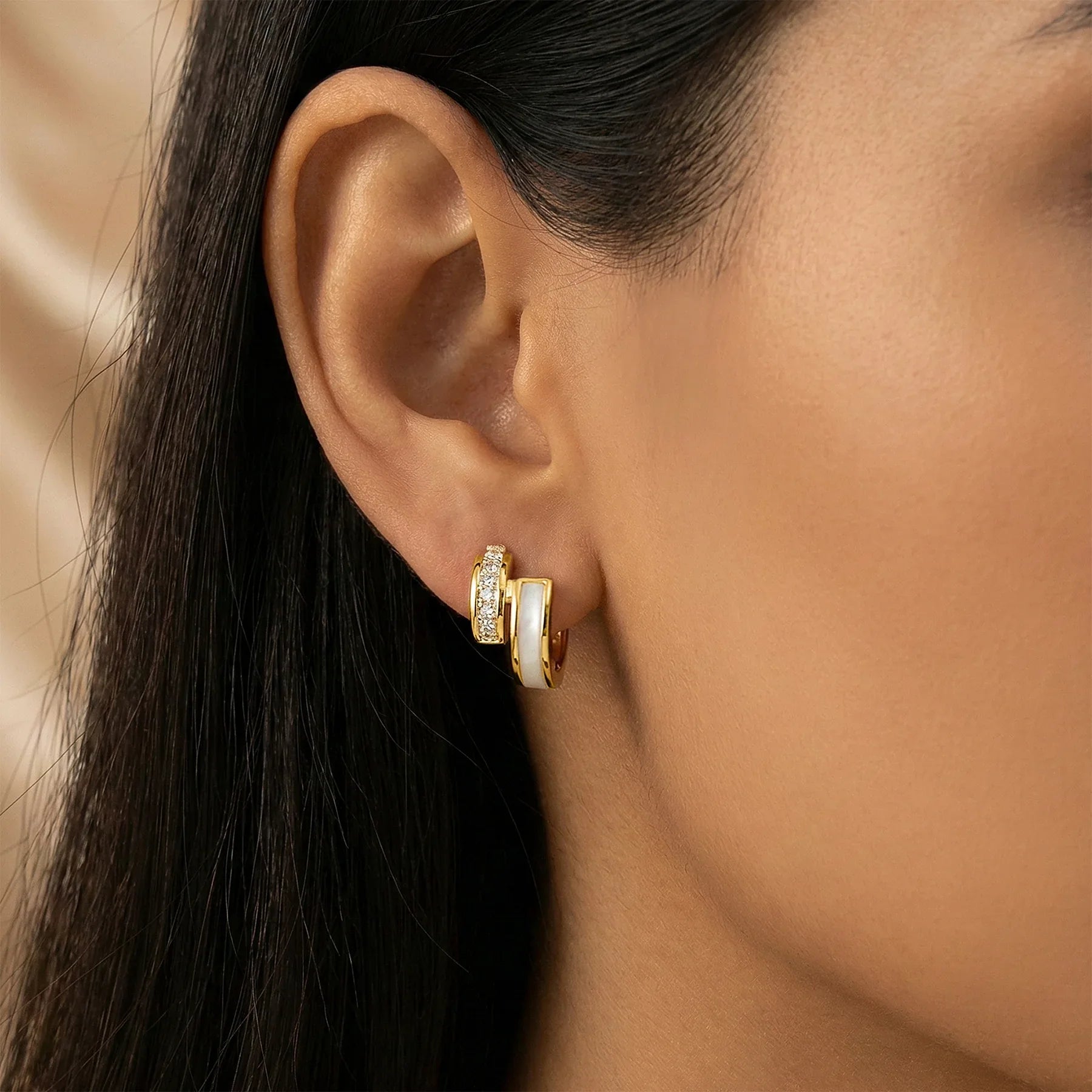 Close-up of a person wearing gold hoop earrings with a neutral background