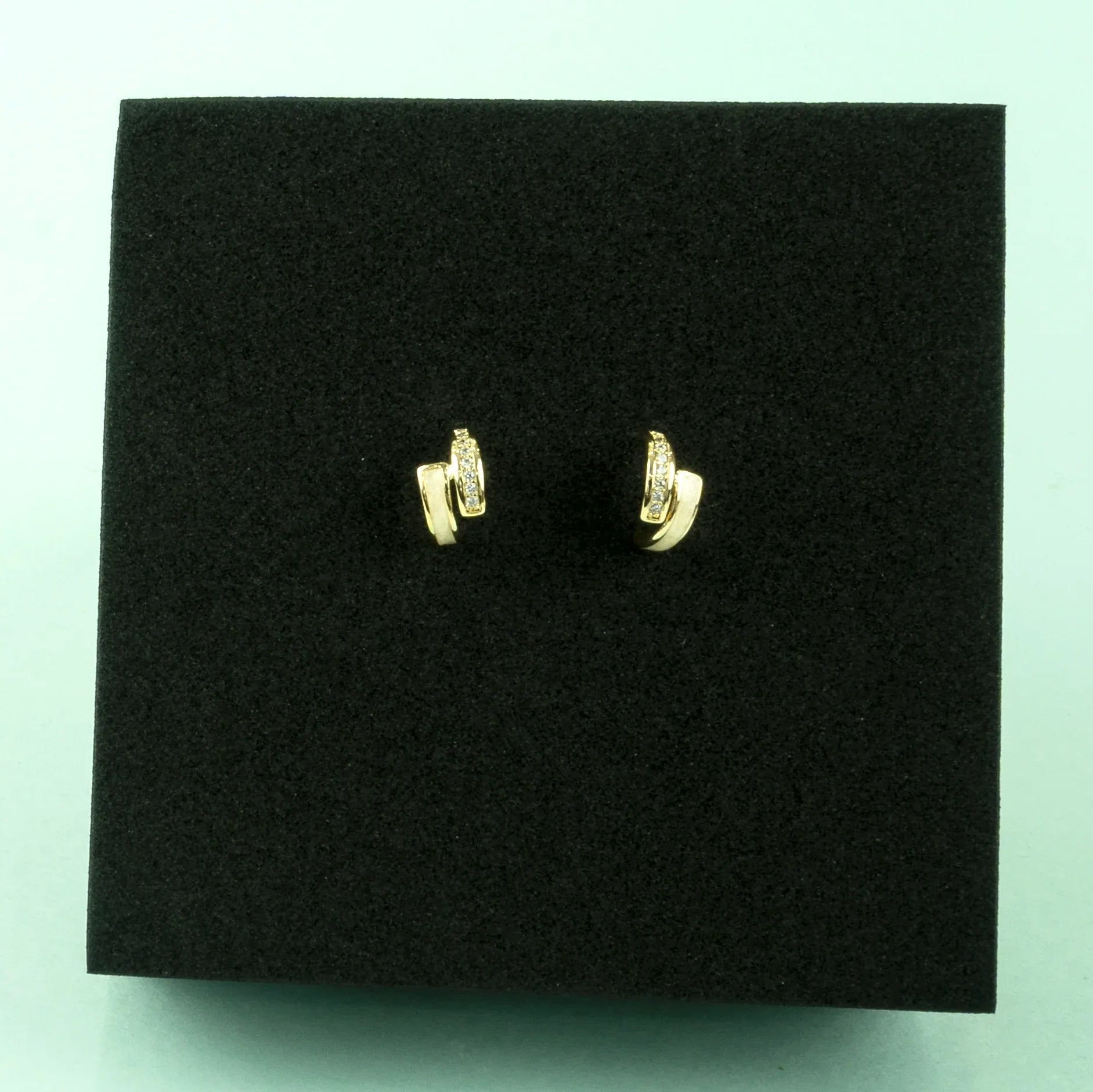 Gold earrings on a black display stand with a light blue background