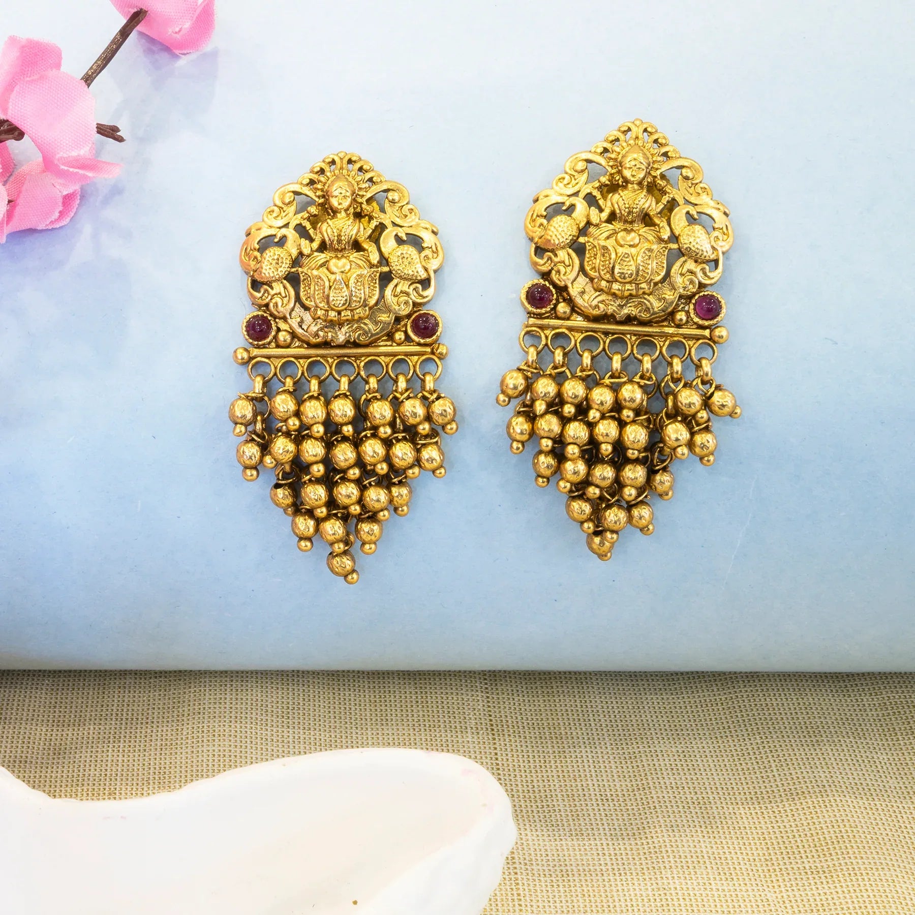 Pair of gold earrings with intricate designs on a light blue background