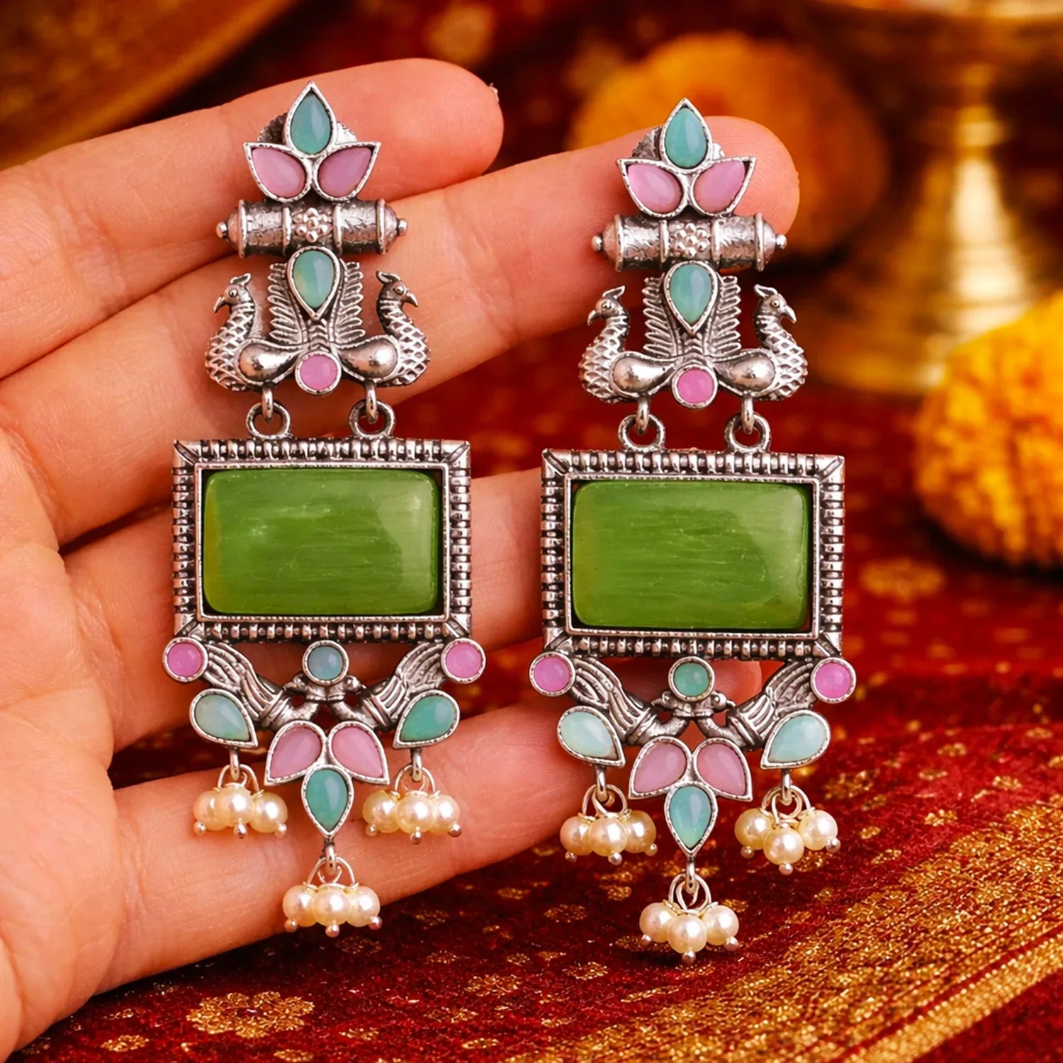 Ornate earrings with green stones held in a hand on a decorative background