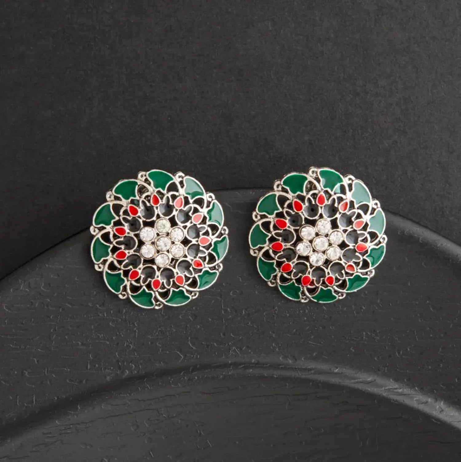 Pair of decorative earrings with green, red, and white design on a black background