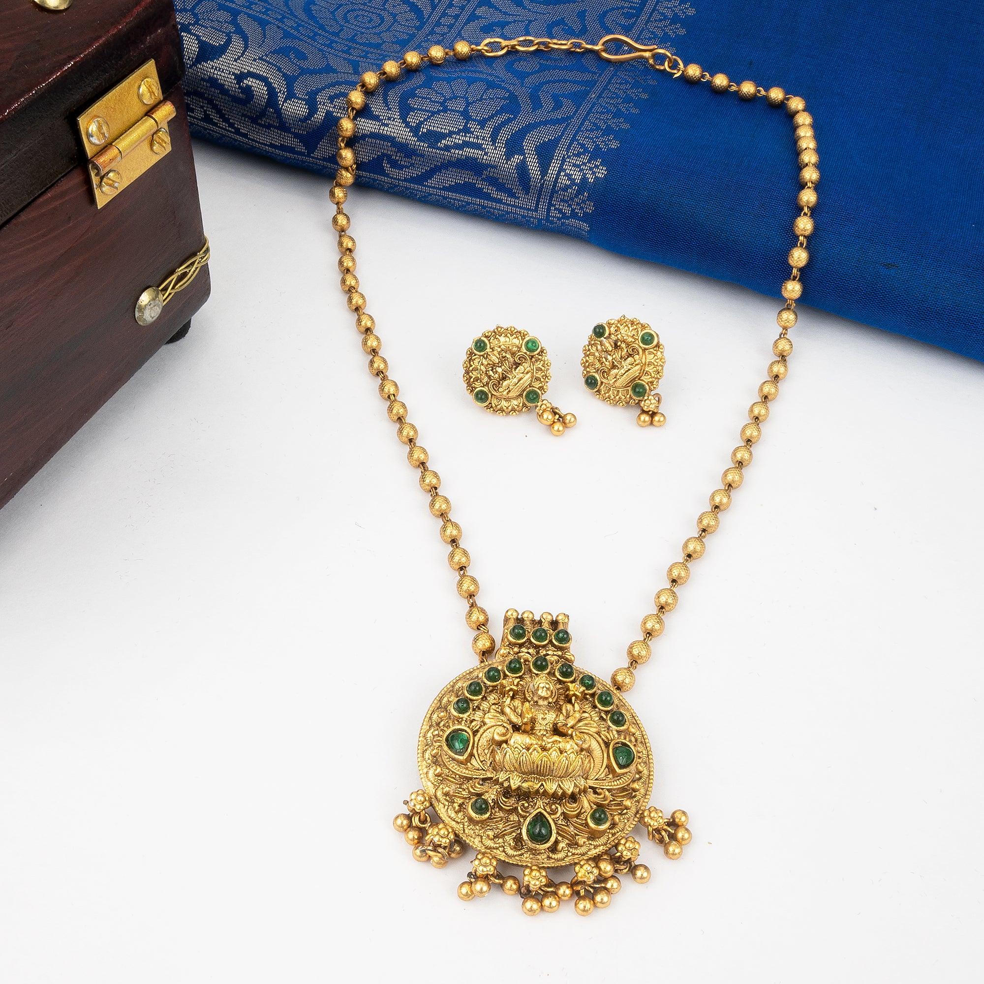 Gold necklace with emerald stones and matching earrings on a white surface with a blue fabric background.