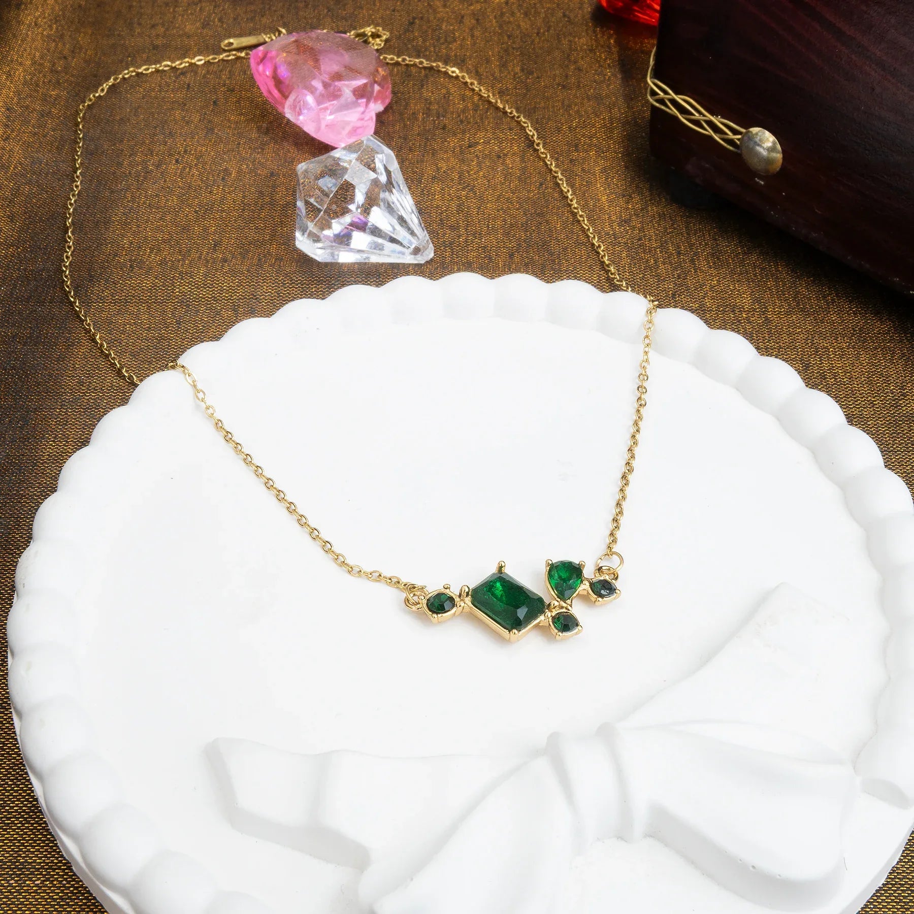 Gold necklace with green gemstones on a white plate with decorative crystals in the background.