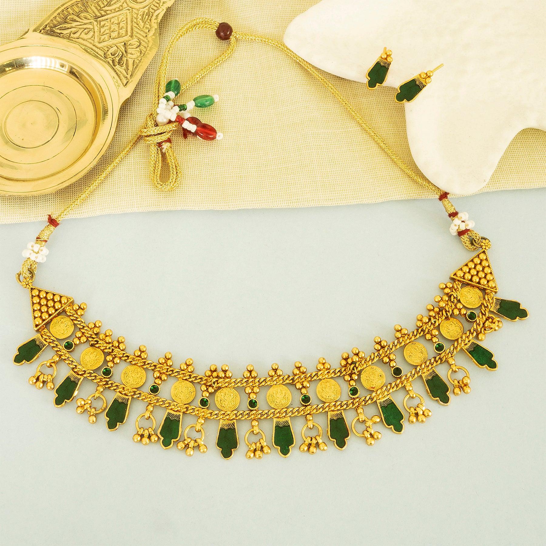 Gold necklace with green and red accents on a light gray background
