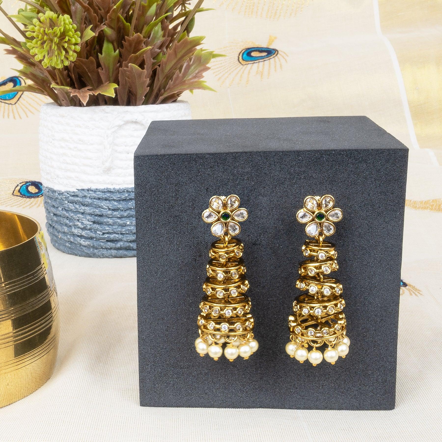 Gold earrings on a gray stand with a plant and decorative item in the background