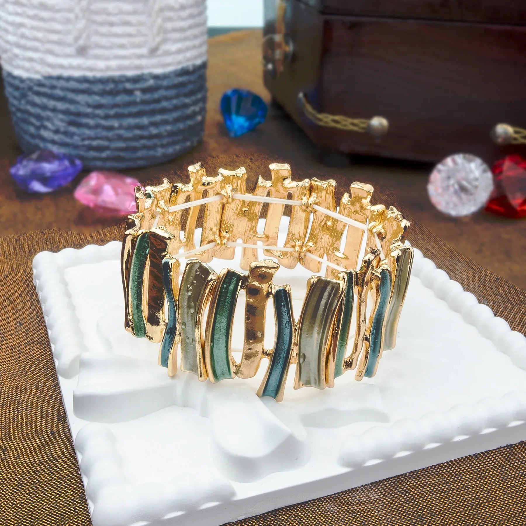 Gold and green bracelet on a white stand with colorful stones in the background