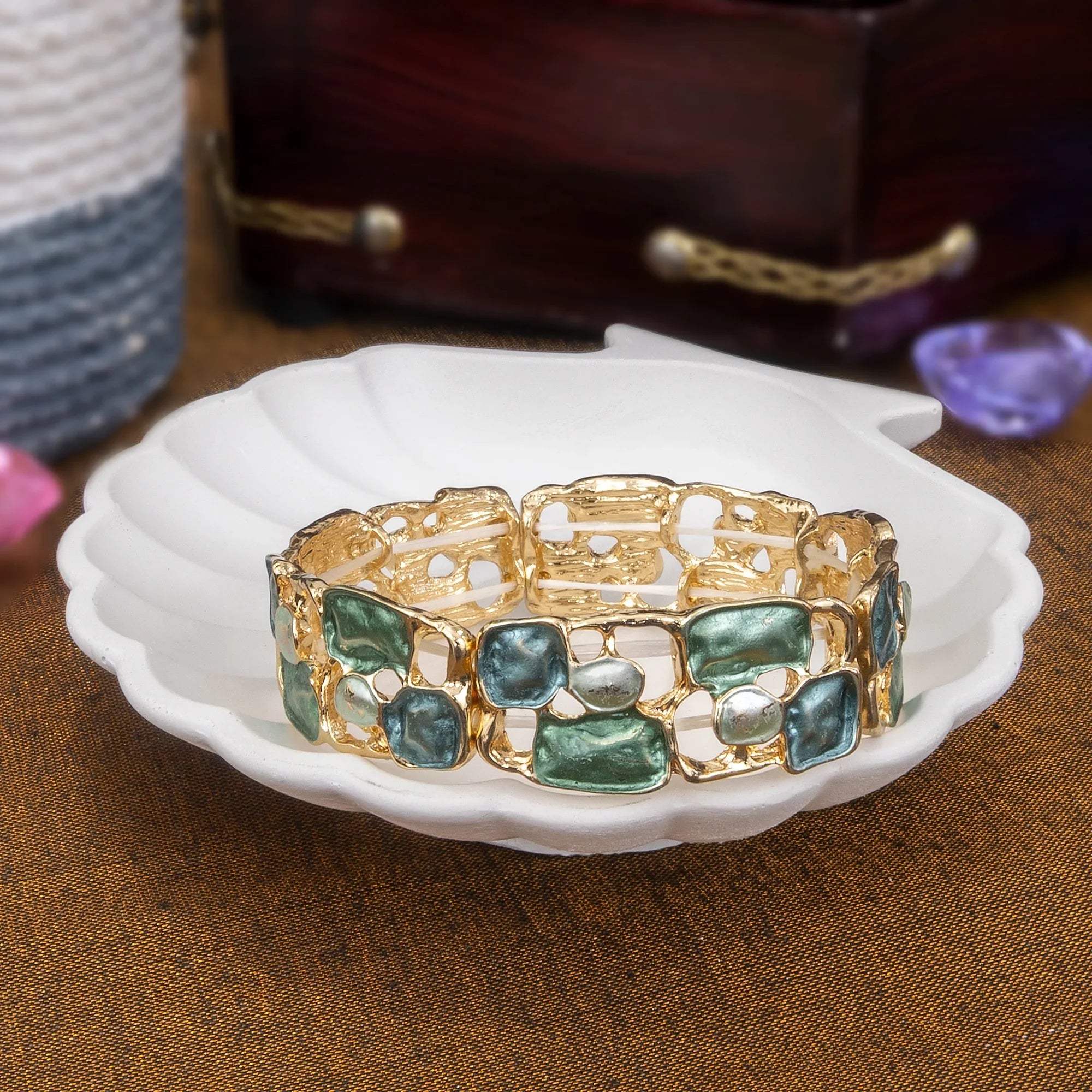 Gold bracelet with green stones on a white dish against a brown background