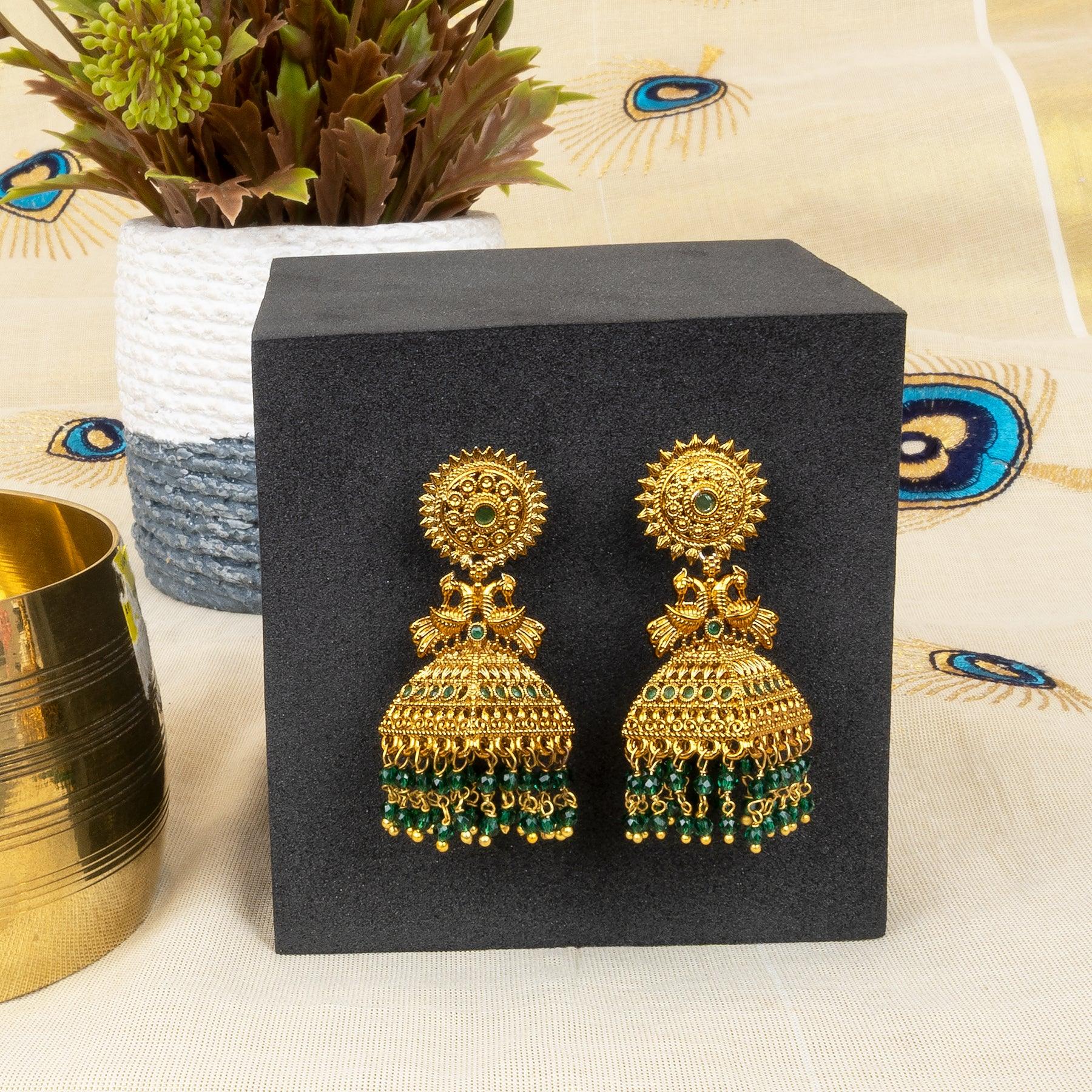 Gold earrings with green beads on a black stand, with a decorative background.