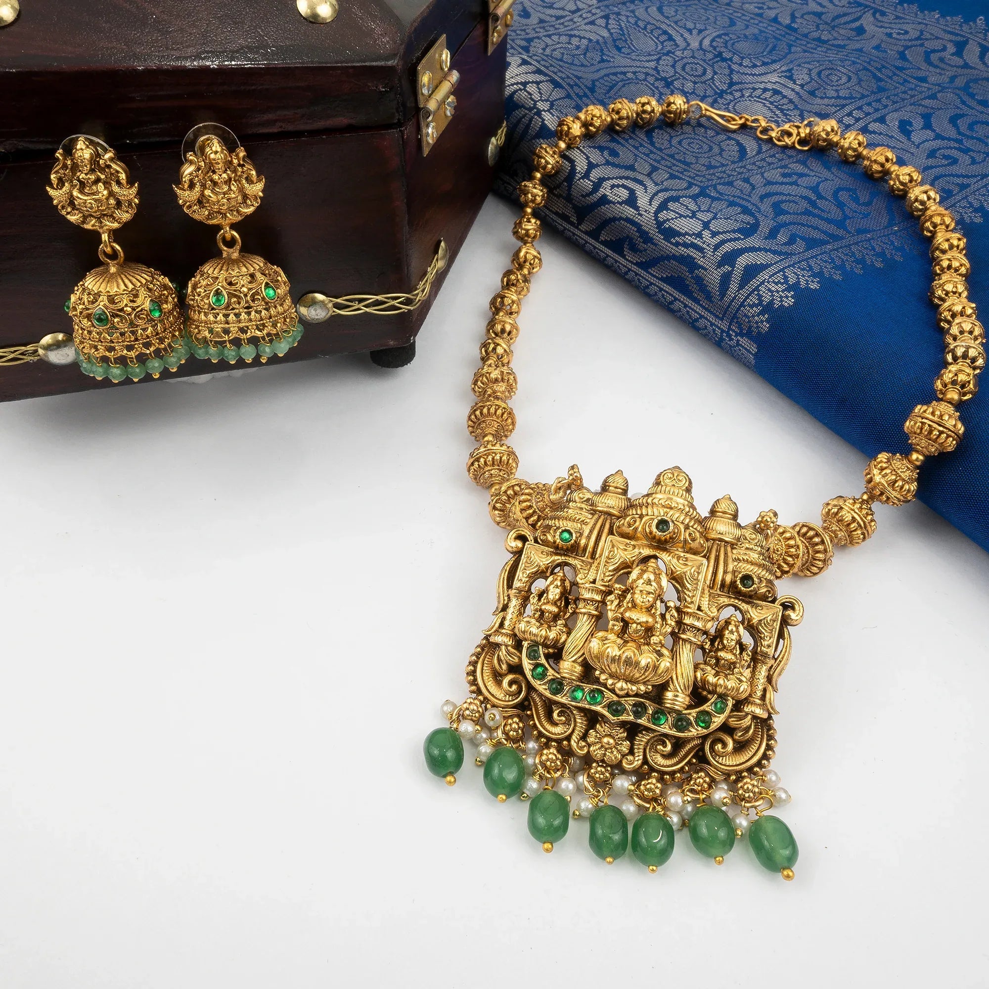 Gold necklace with green gemstones on a white surface with a blue fabric background