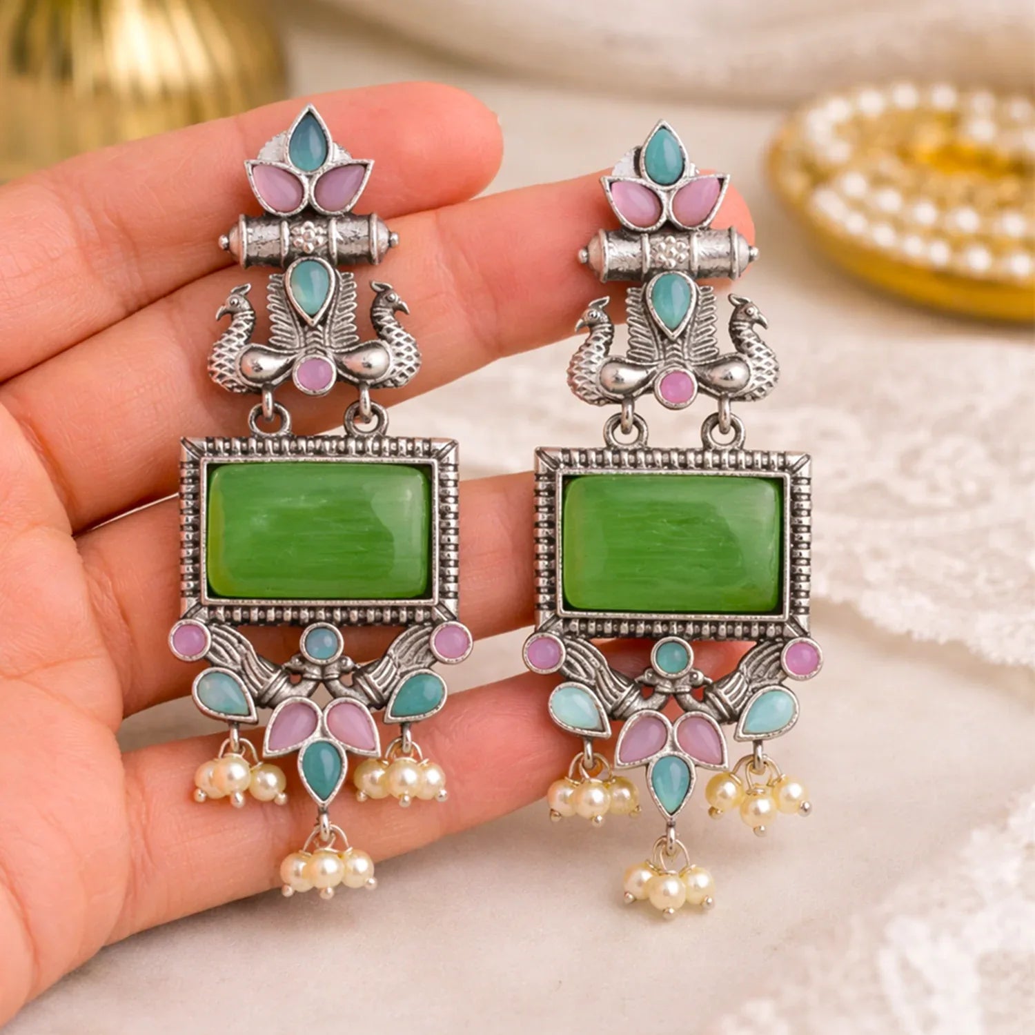Decorative earrings with green stones and pearl-like beads held in a hand.