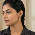 Woman wearing gold earrings with green stones against a neutral background