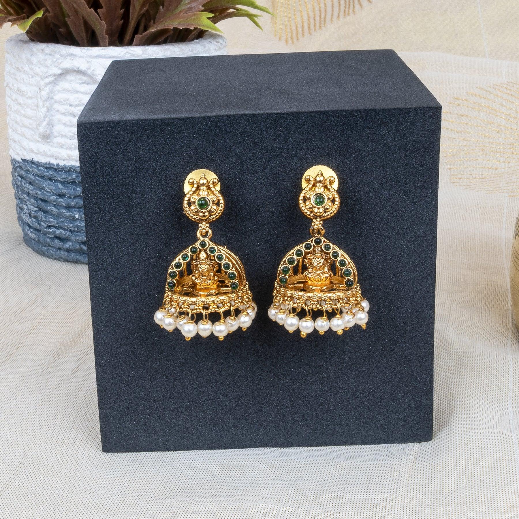 Gold and pearl earrings on a black stand with a blurred background