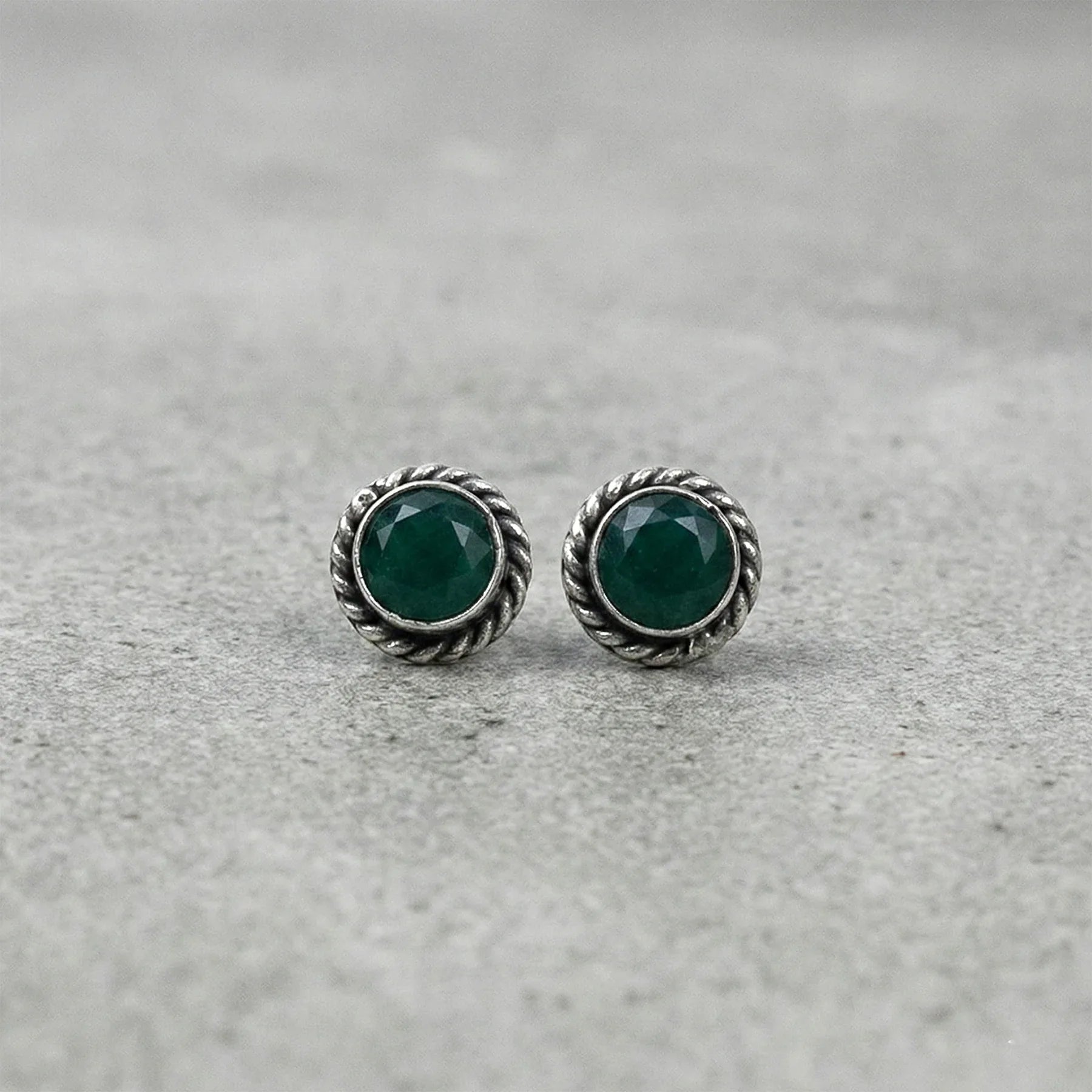 Pair of silver earrings with green gemstones on a gray background