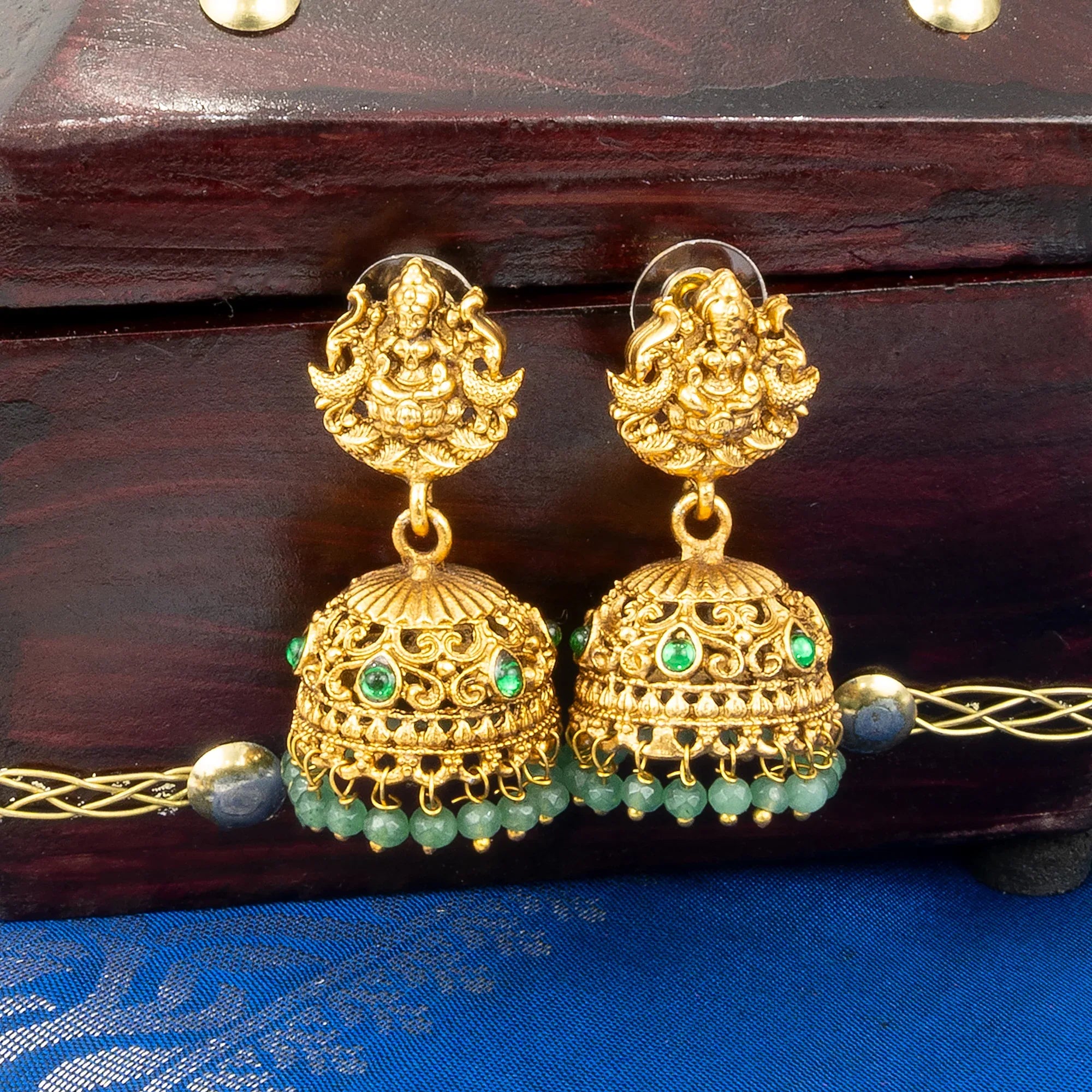 Gold earrings with green beads on a wooden box