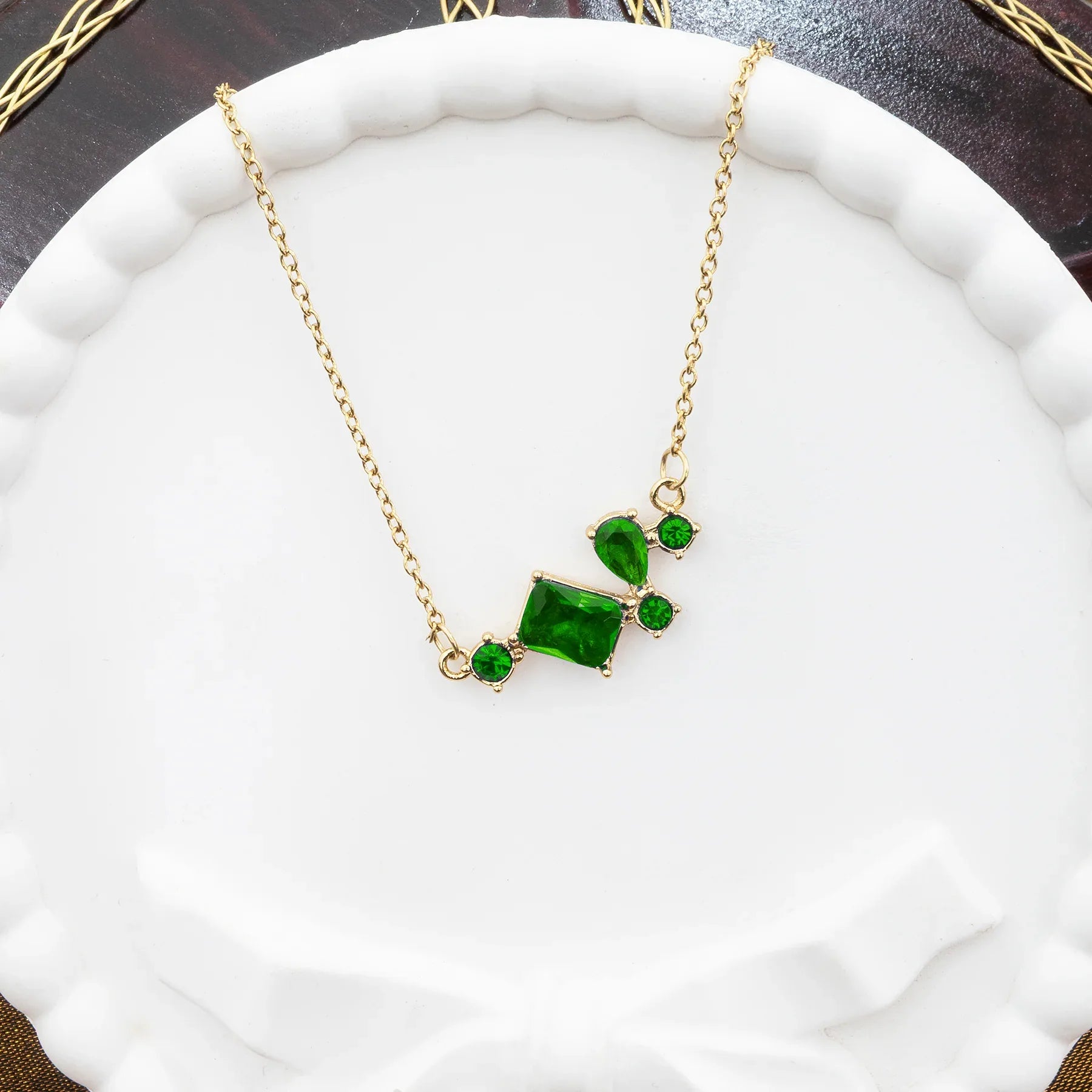 Gold necklace with green gemstones on a white cushion