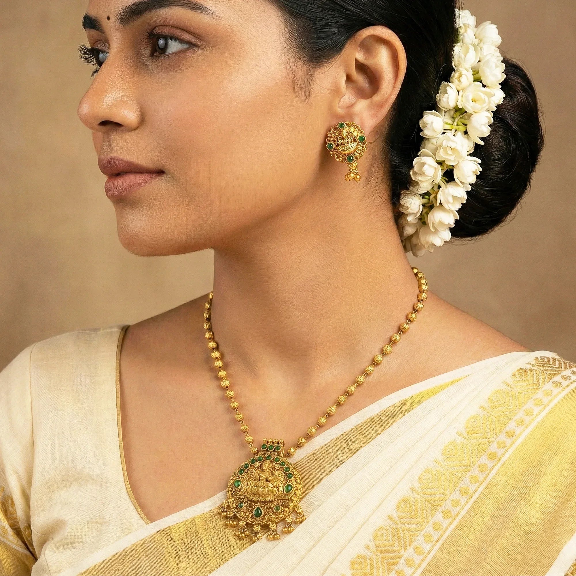 Woman wearing gold jewelry including a necklace and earrings, with a neutral background