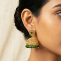 Gold and green earrings worn by a person with a neutral background