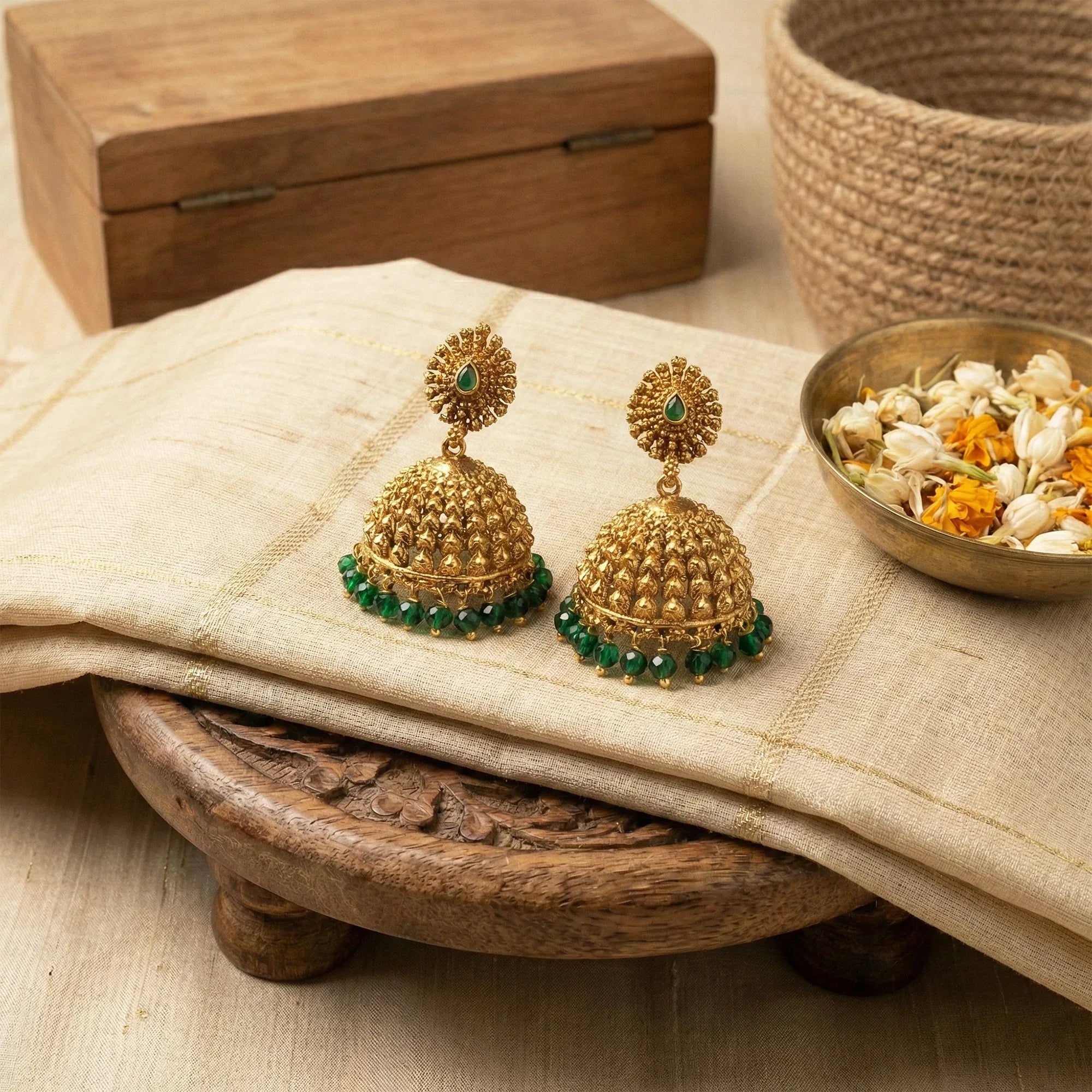 Gold earrings with green gemstones on a wooden tray with fabric and decorative elements.