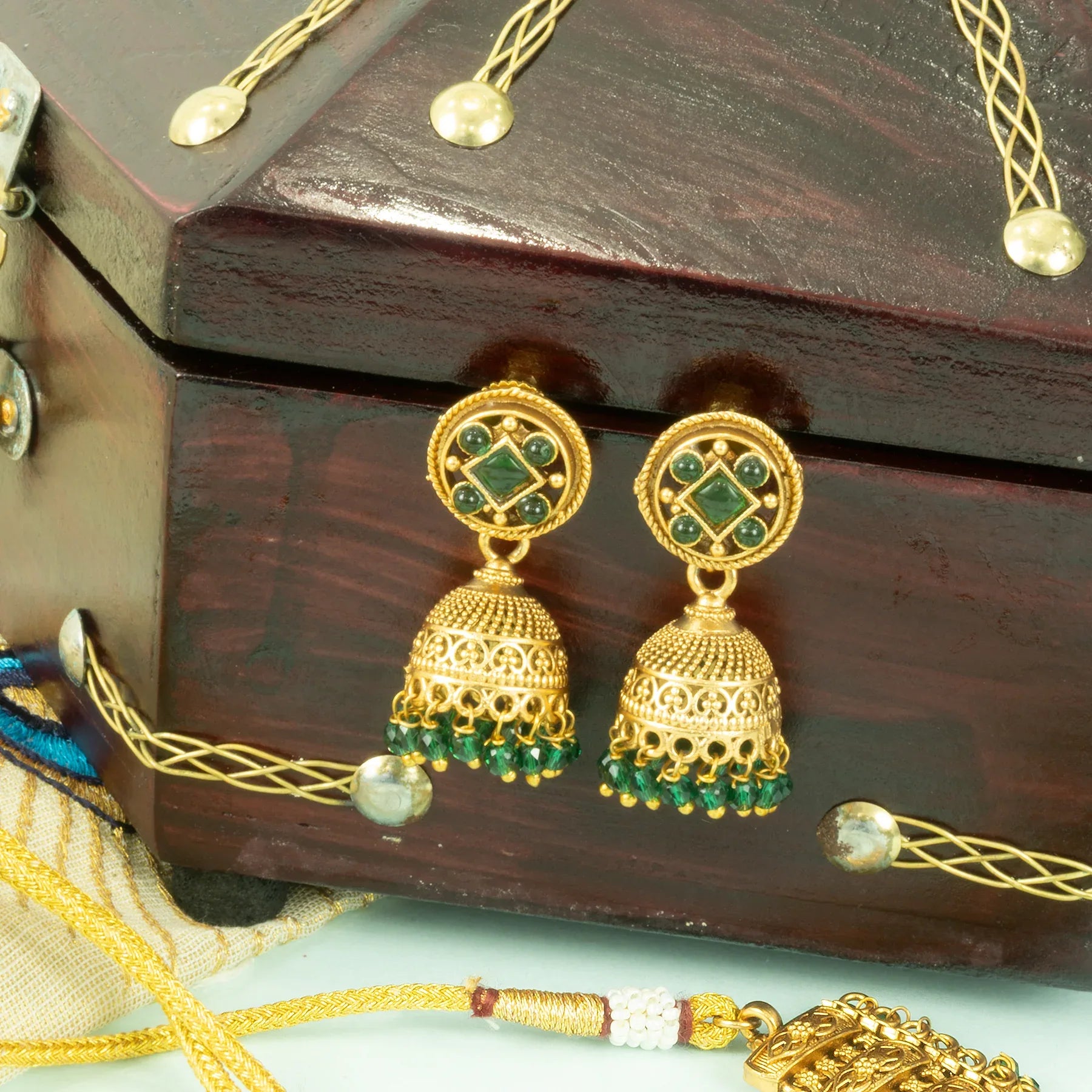 Gold and green earrings on a wooden jewelry box with decorative strings.