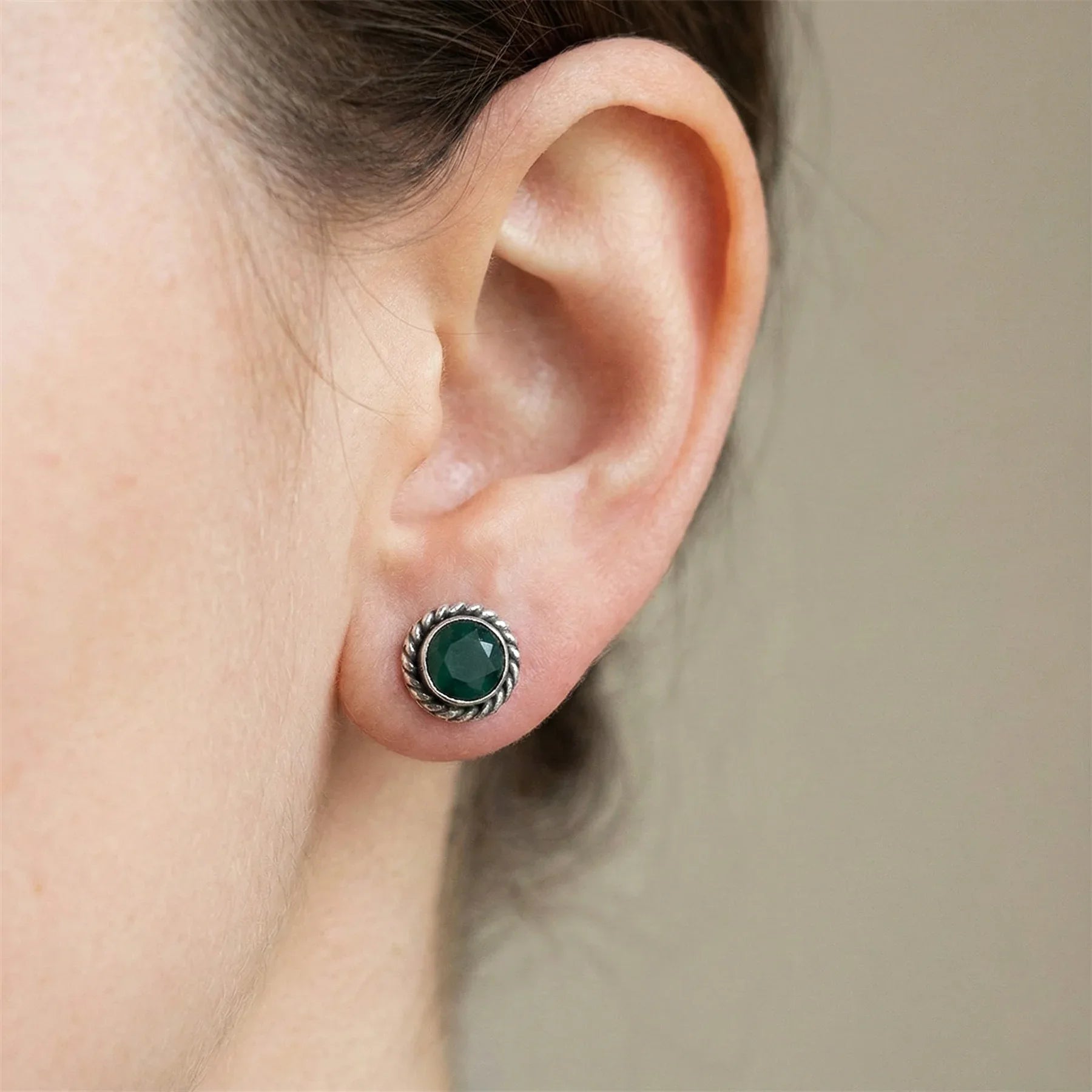 Close-up of an ear wearing a green gemstone earring with a silver setting.