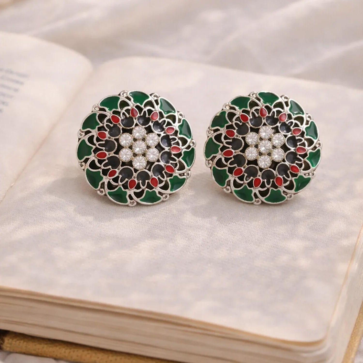 Pair of decorative earrings with green, black, and red design on a white fabric background