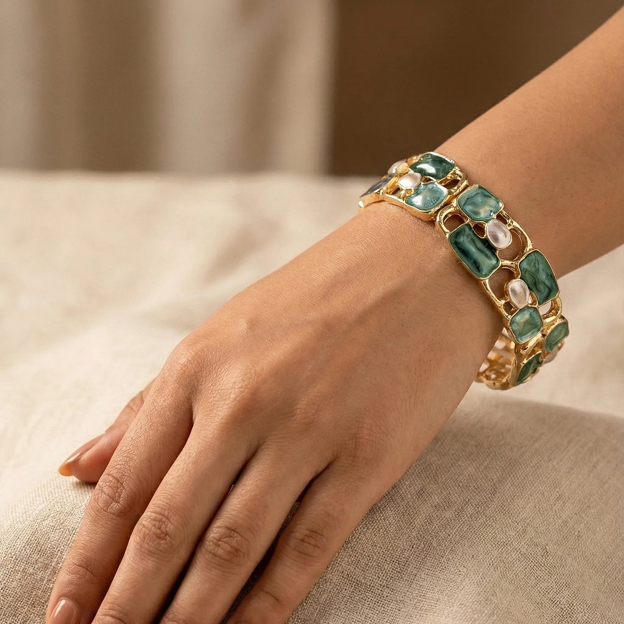 Gold bracelet with green gemstones on a hand against a neutral background