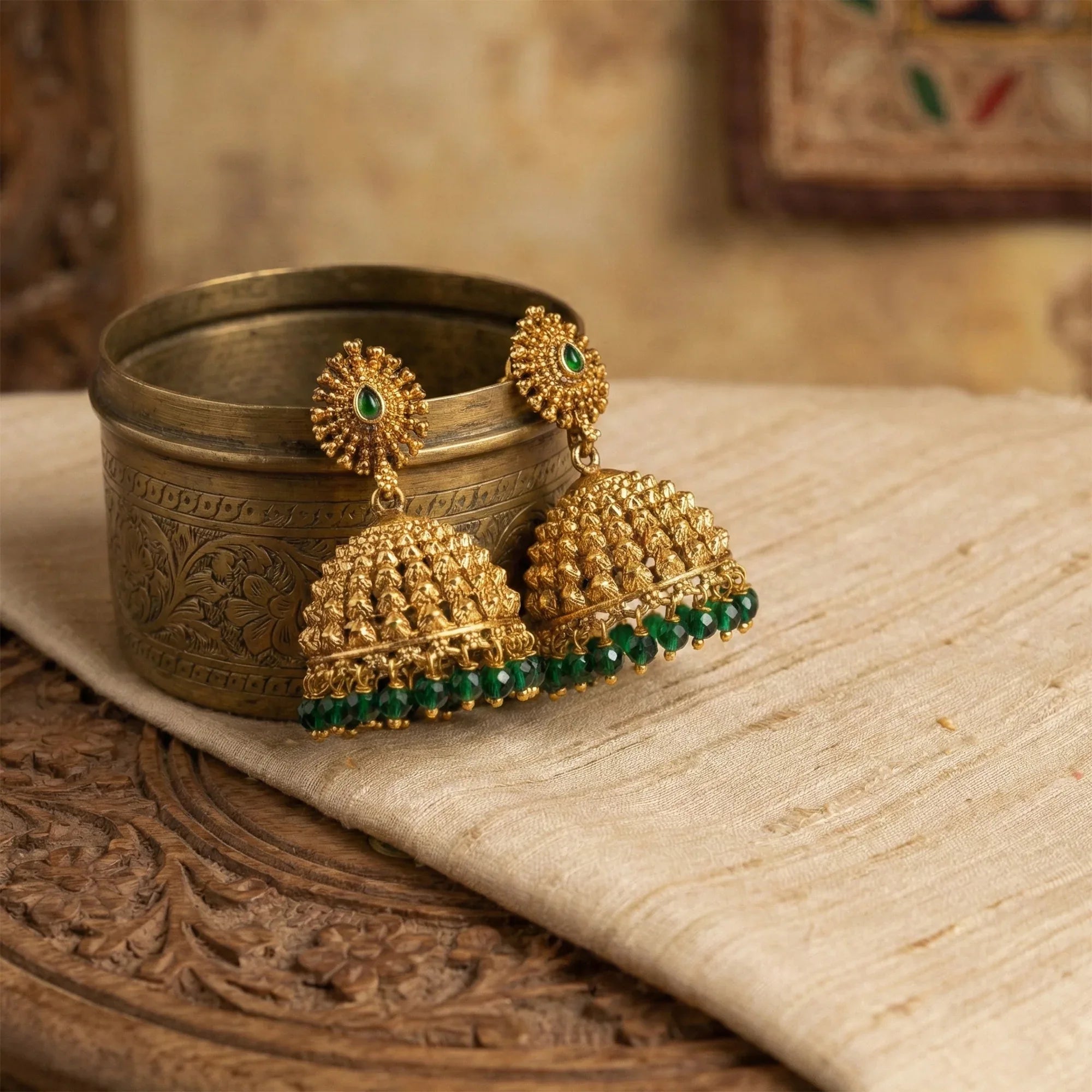 Gold earrings with green gemstones on a decorative surface
