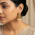 Close-up of a woman wearing gold earrings with green gemstones against a neutral background
