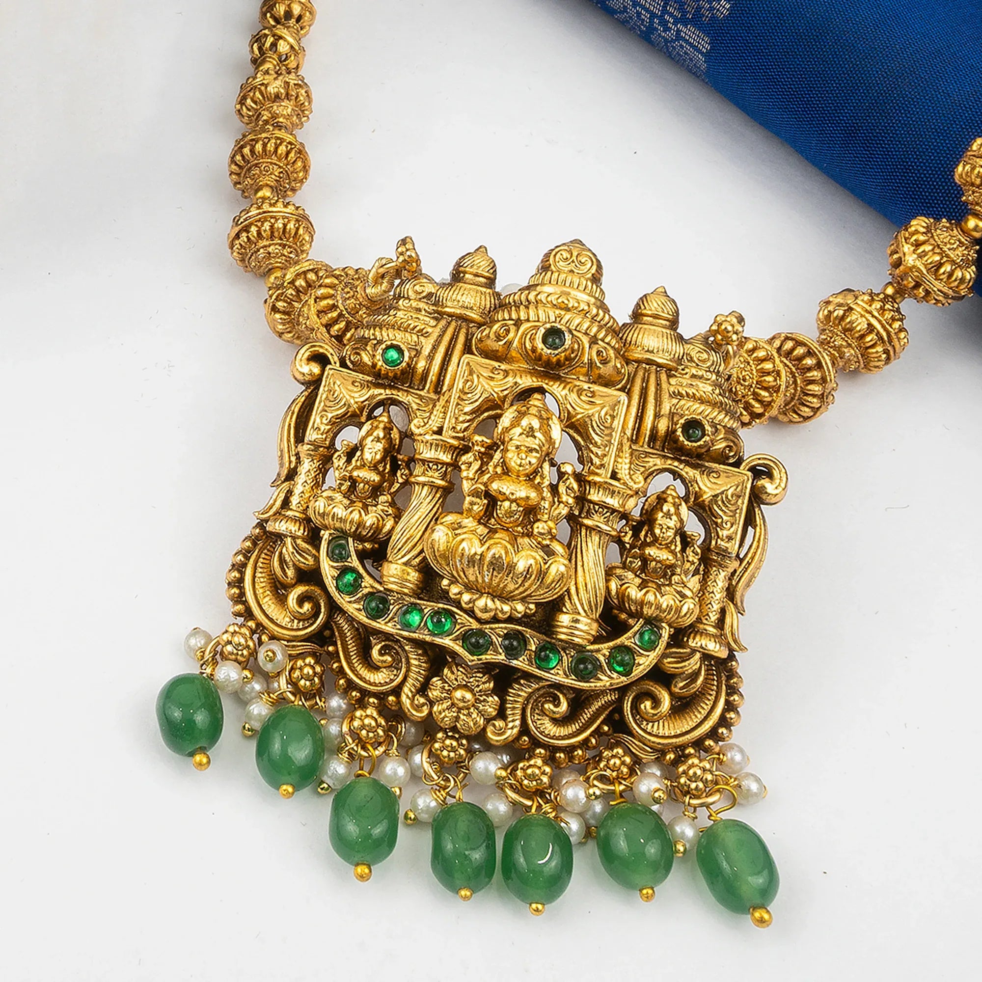 Gold necklace with green gemstones and white pearls on a white background