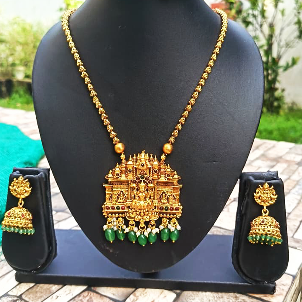 Gold necklace with green gemstones and matching earrings on a black stand outdoors.