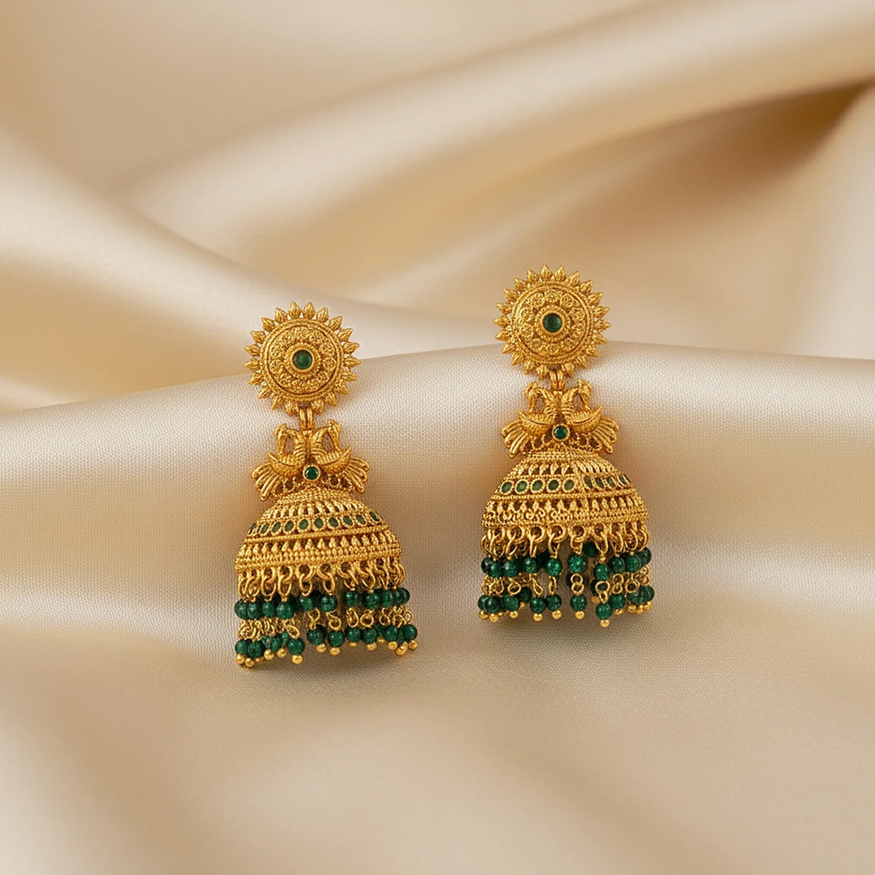 Gold earrings with green gemstones on a beige fabric background
