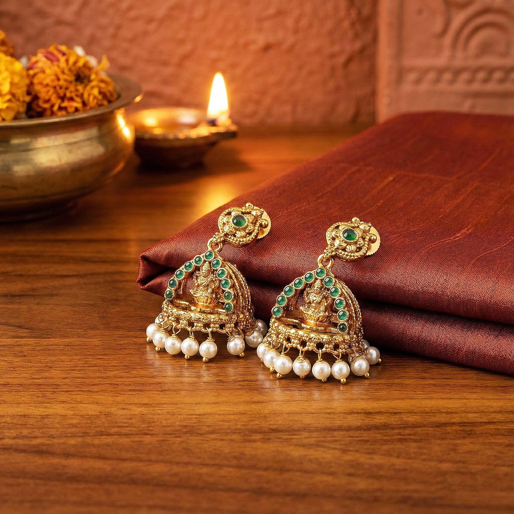 Gold earrings with green stones and pearls on a wooden surface with decorative elements.