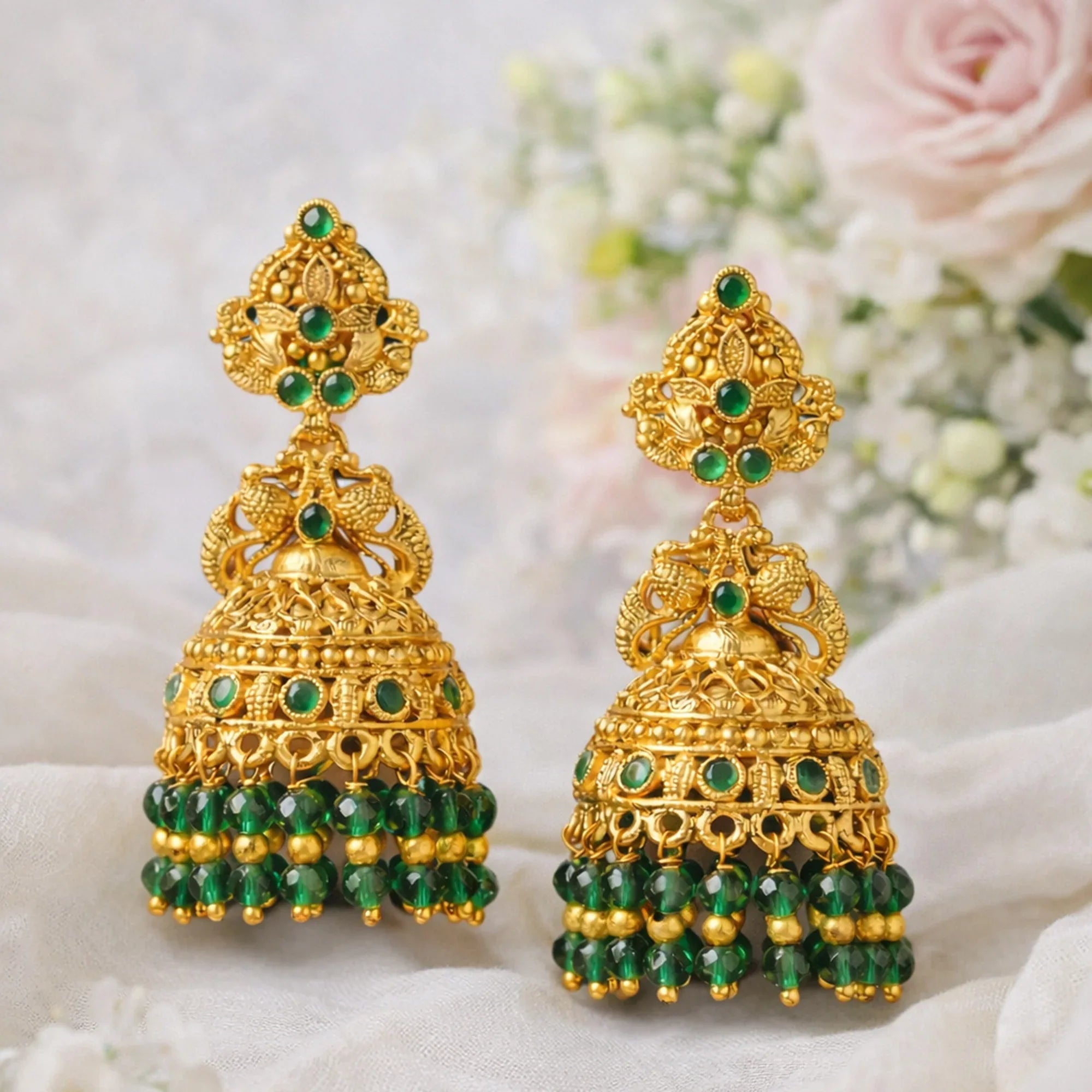 Gold and green beaded earrings on a soft white background with flowers.
