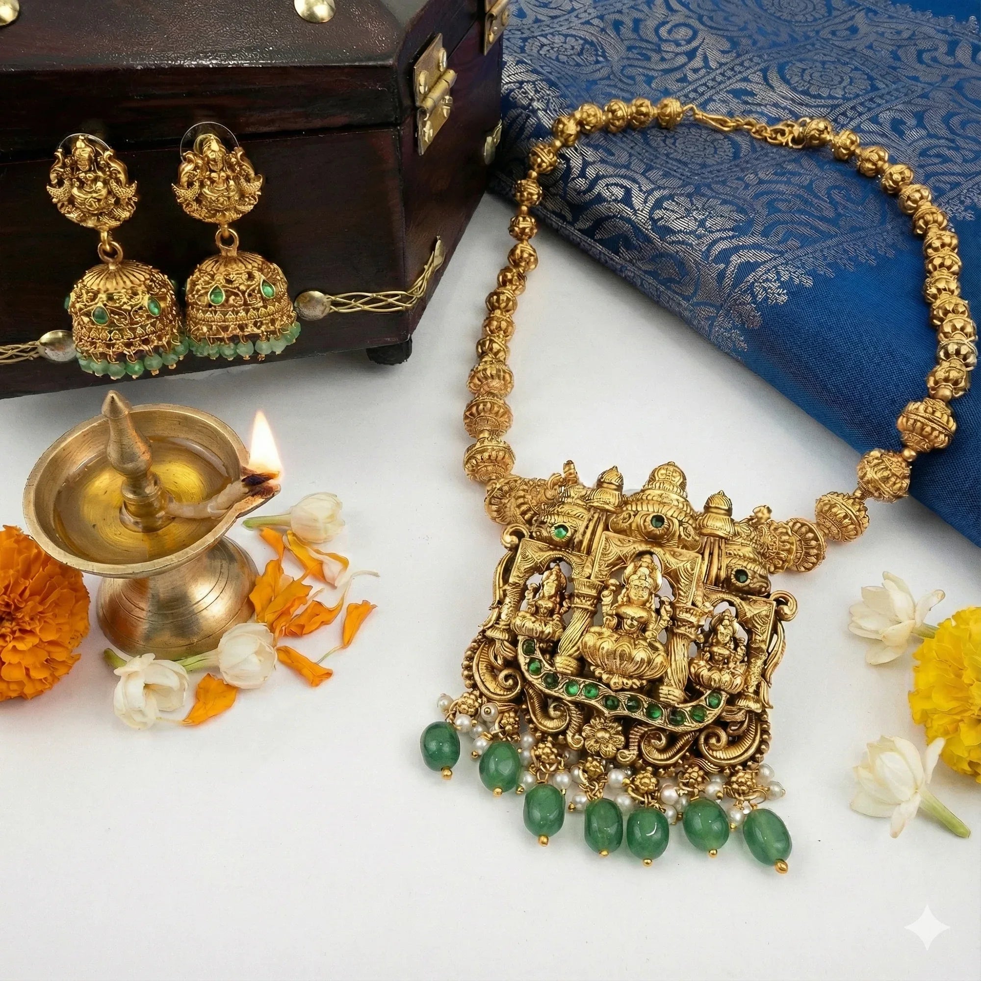 Gold necklace with green gemstones and earrings on a white surface with decorative elements.