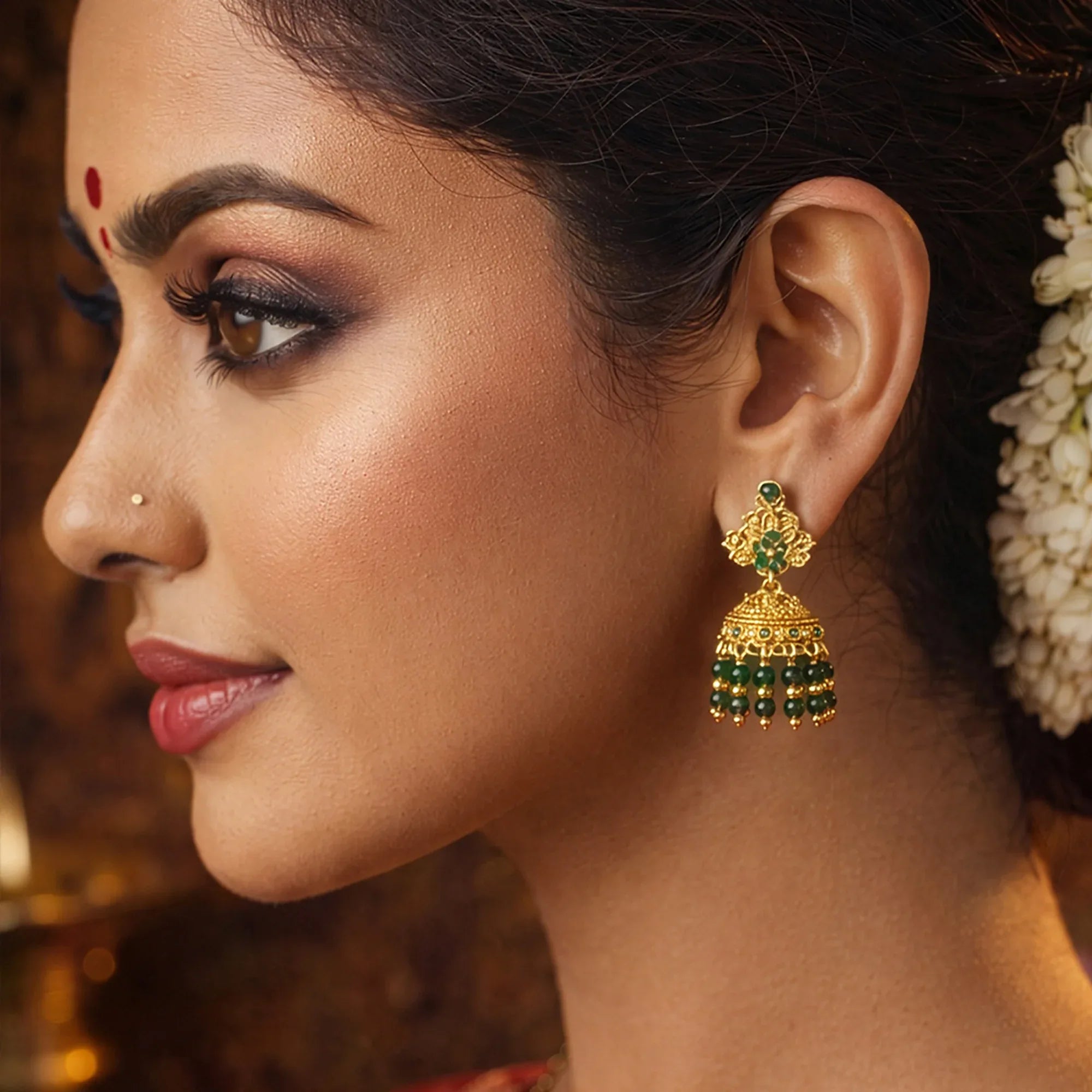 Close-up of a woman wearing gold and green earrings with a blurred background
