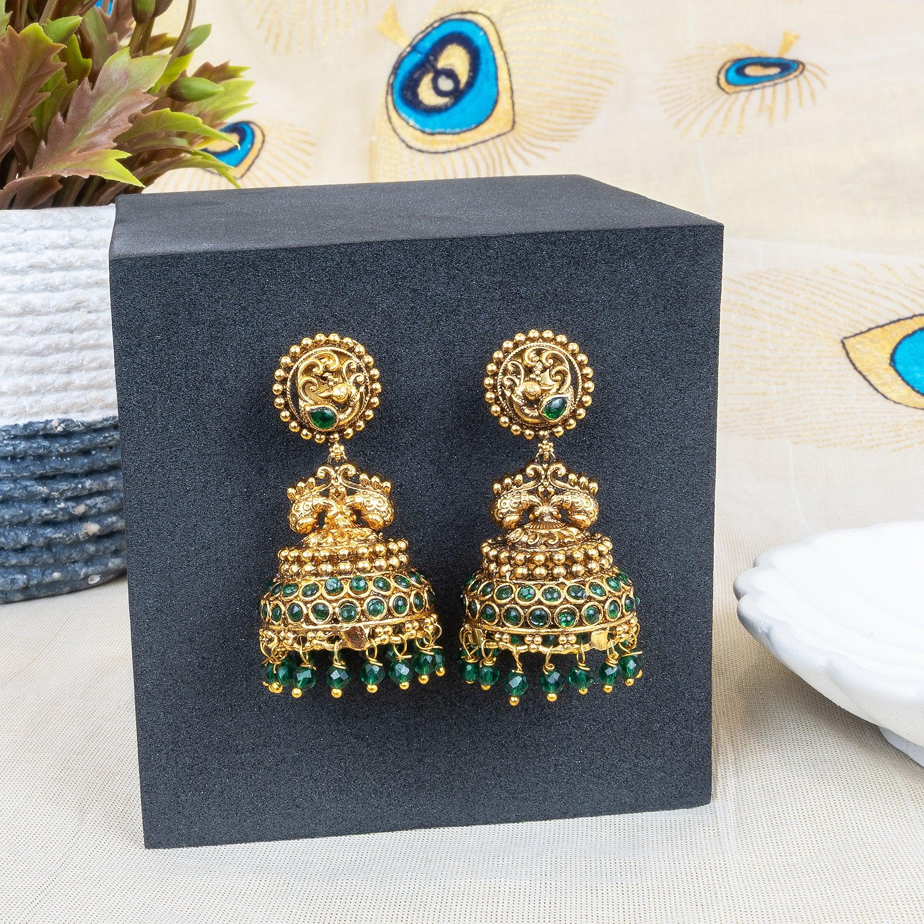 Gold and green earrings on a black stand with decorative background