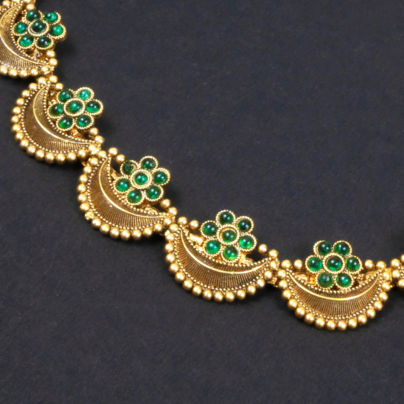Gold necklace with green gemstones on a dark background