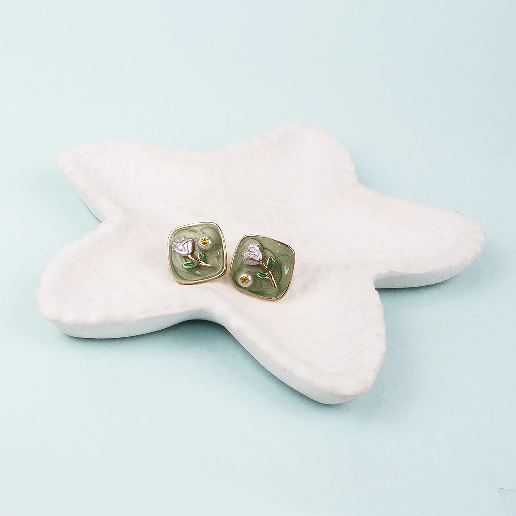 Pair of floral earrings on a star-shaped white stone with a light blue background