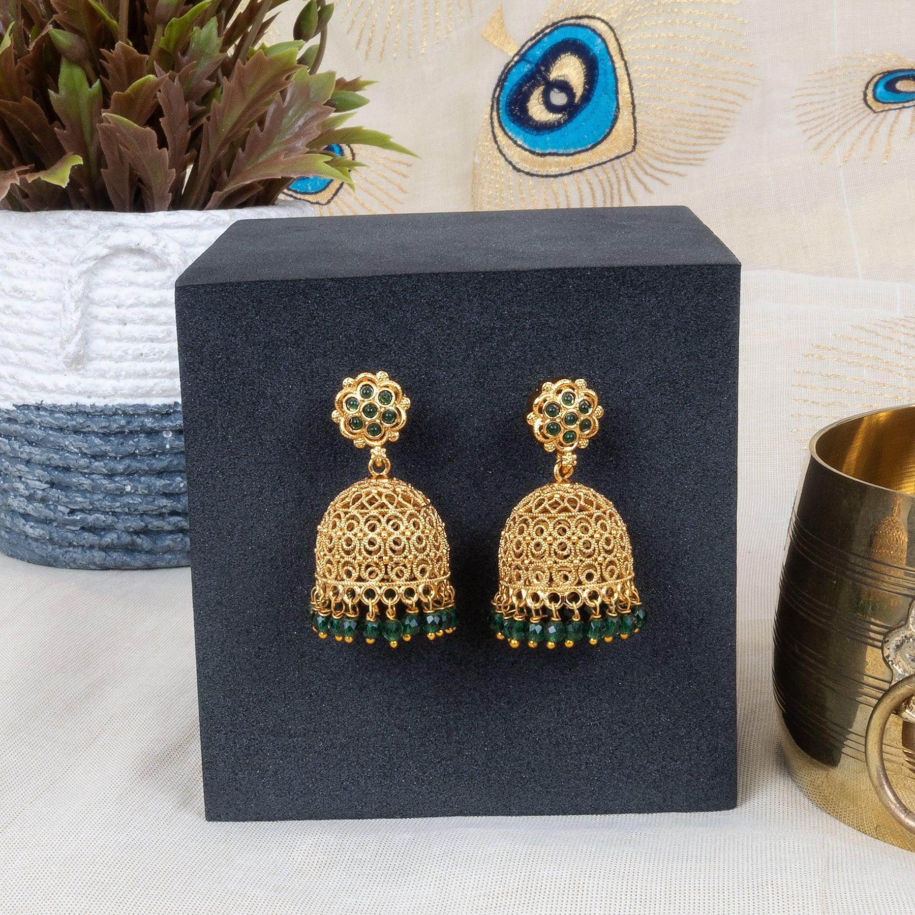 Gold and green earrings on a black stand with decorative background