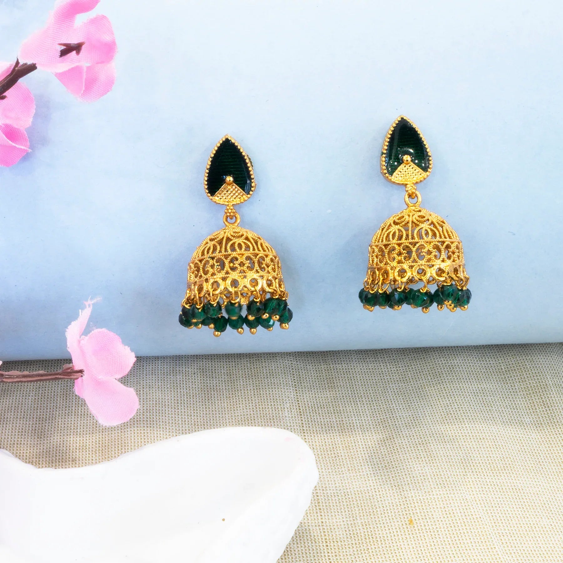 Gold and green earrings on a light blue background with pink flowers.