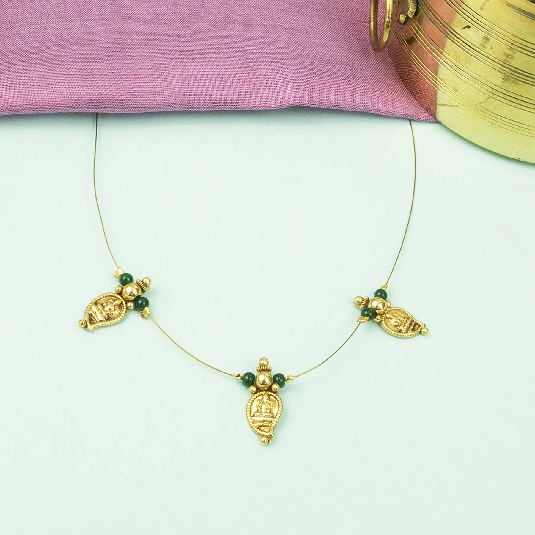 Gold necklace with green beads on a light pink fabric background