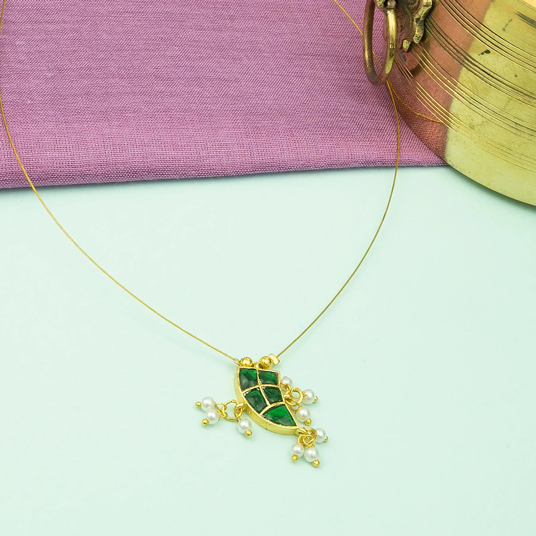 Gold necklace with a green pendant and pearl accents on a light green background