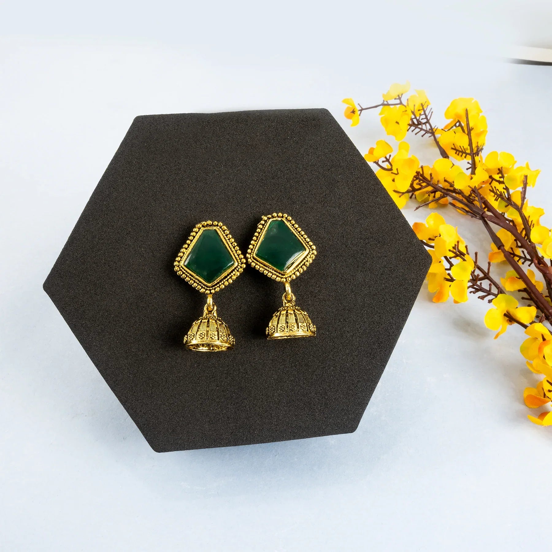Gold and green earrings on a black hexagonal stand with yellow flowers.